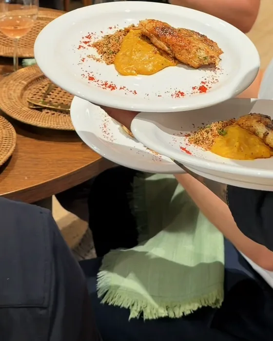 Pratos de peixe grelhado com purê alaranjado e farofa sendo levados à mesa.