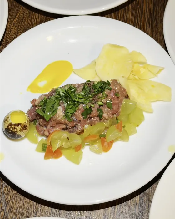 Tartare com vinagrete verde, chips de mandioquinha e creme de pequi num prato branco.